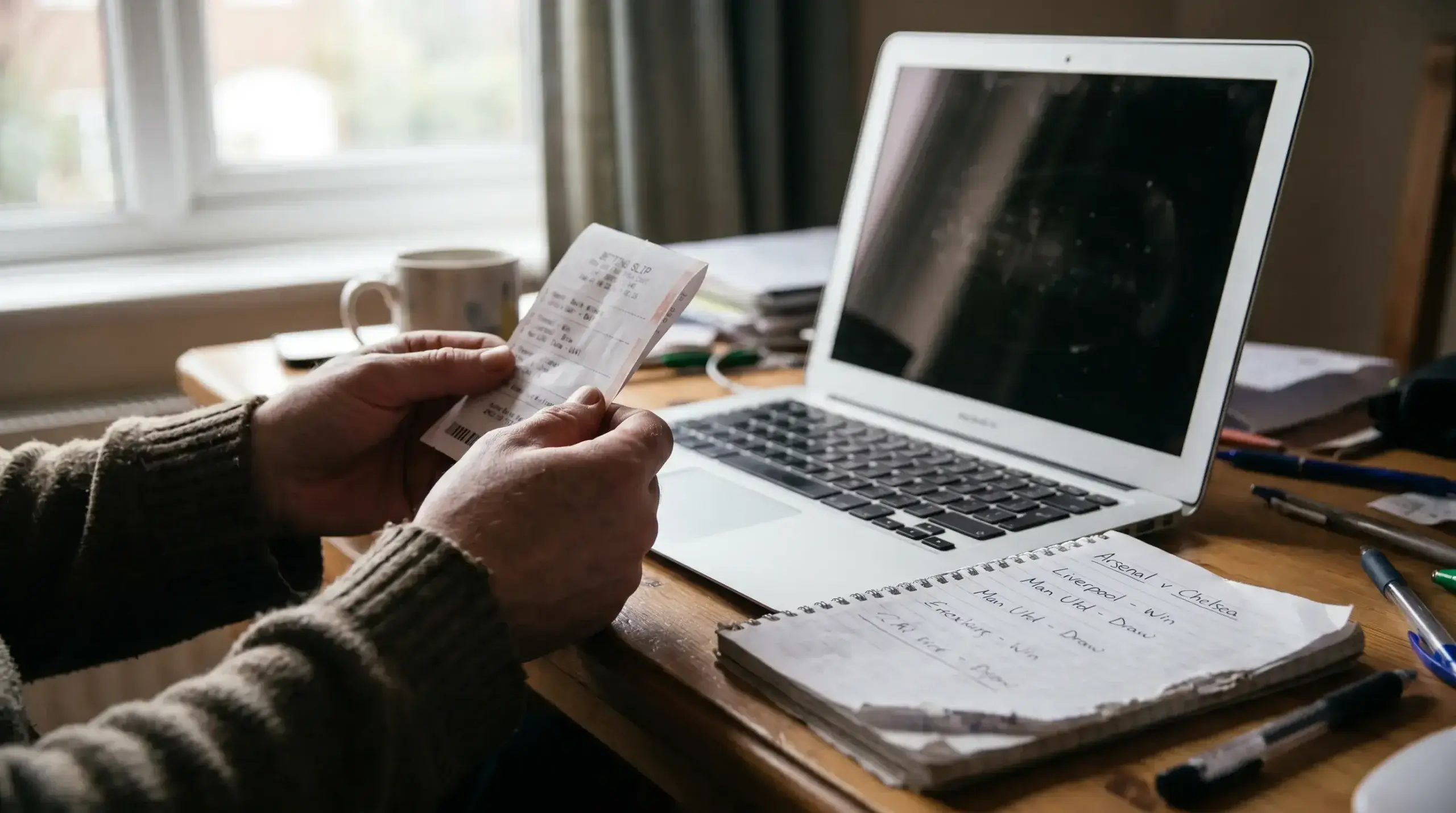 Hands holding a printed paper slip beside a laptop on a wooden desk