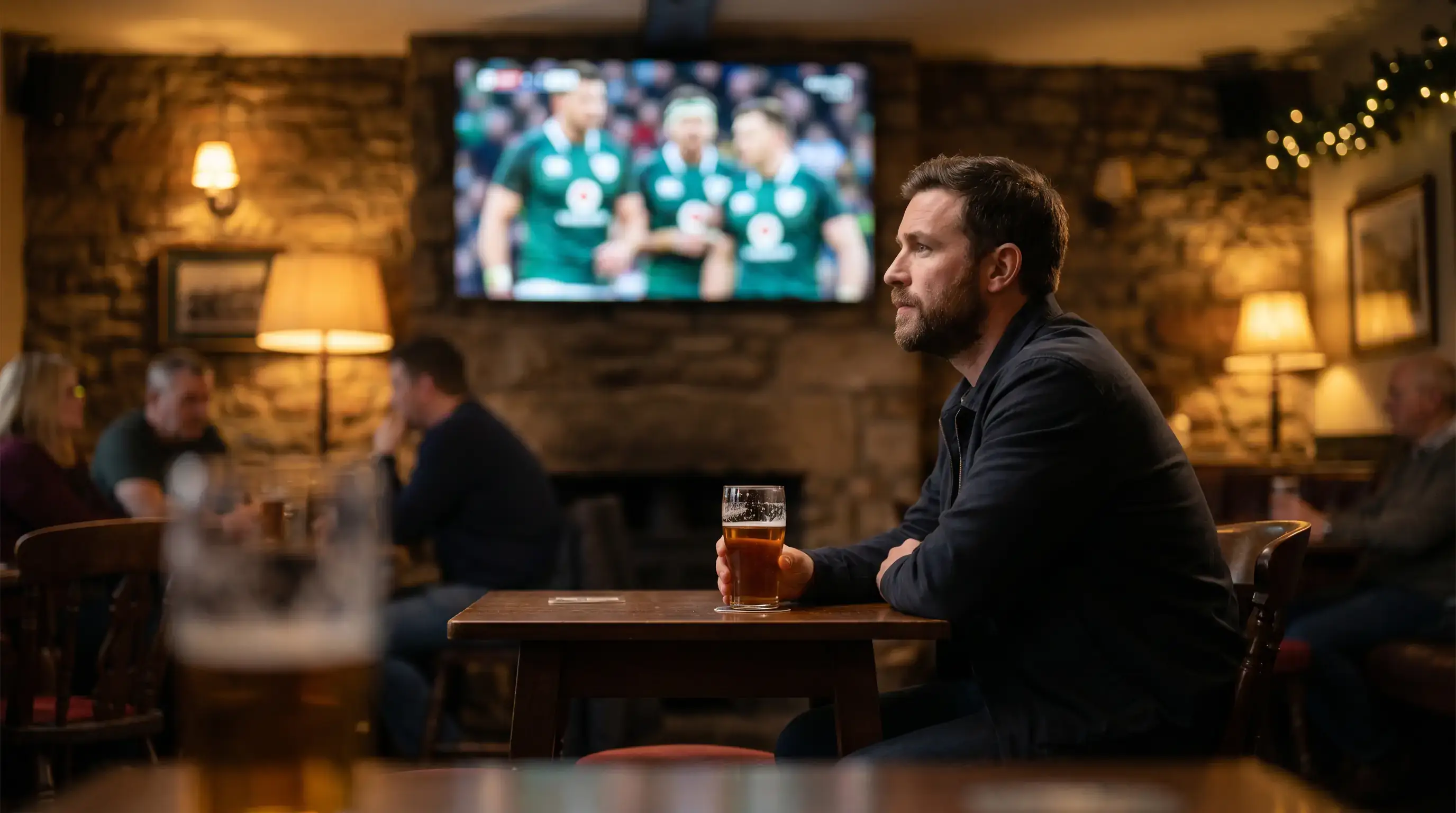 A bettor in a UK pub watching a rugby match on a wall screen with a pint