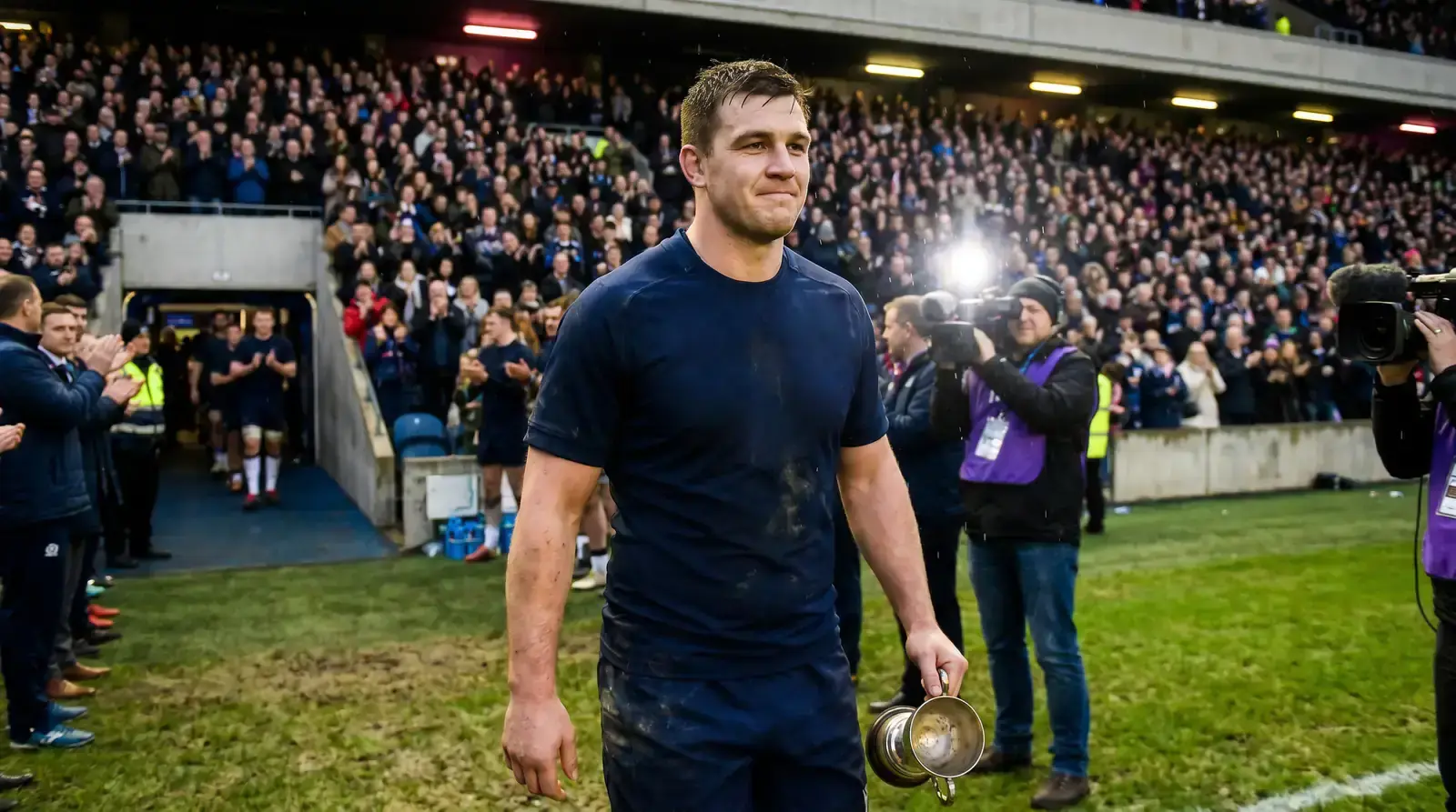 Rugby player walking off the pitch to applause with a tournament award trophy