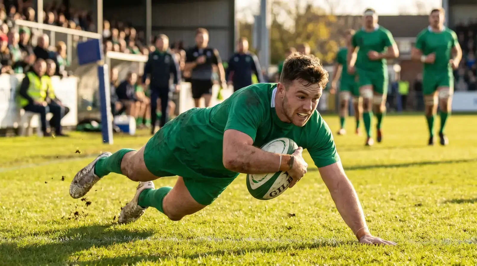 Rugby winger diving over the try line on a sunlit pitch